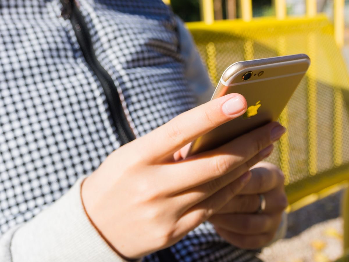 Close-up of a hand checking a phone outdoors by a yellow railing