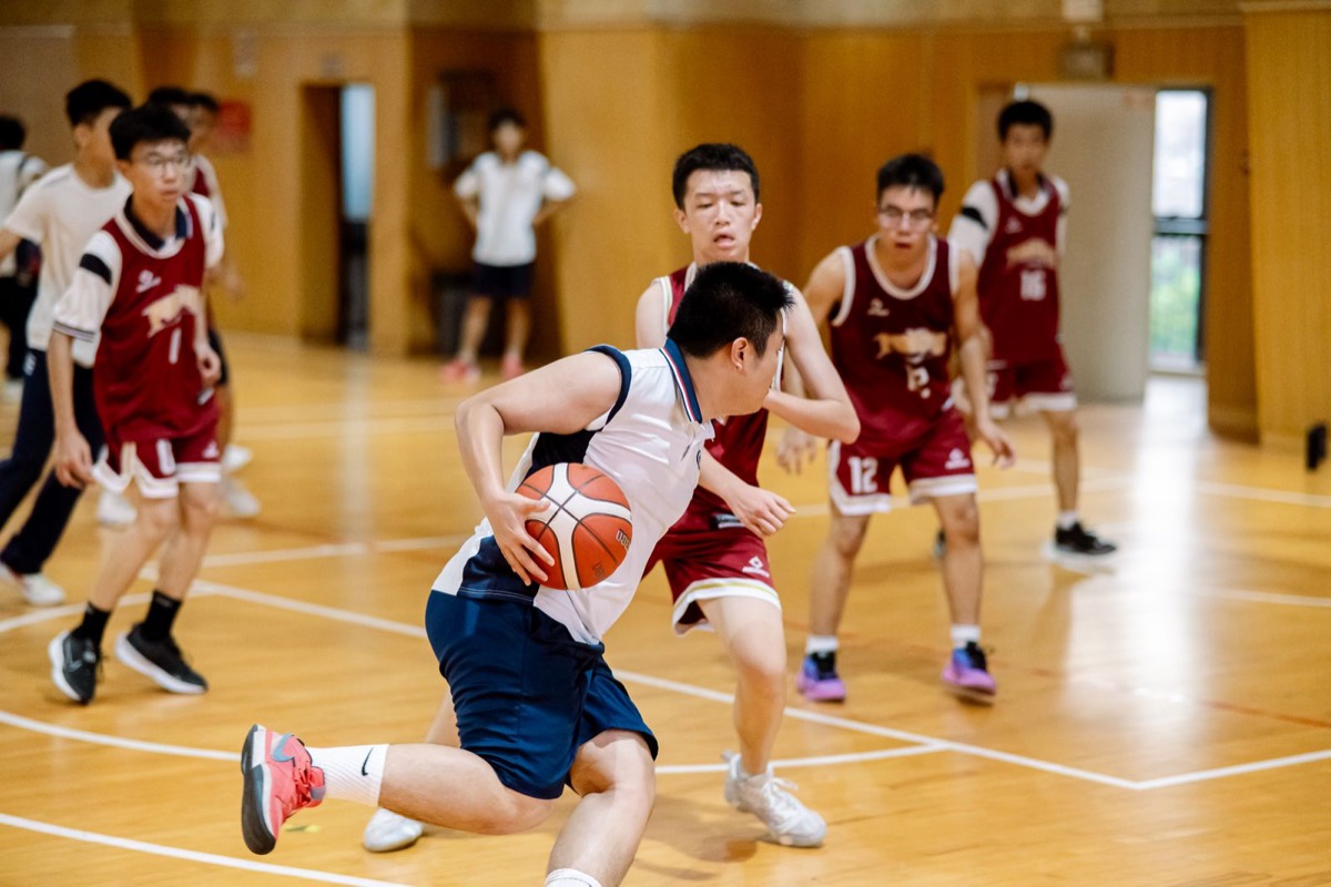 Teenage player driving with the ball as defenders converge in a gym