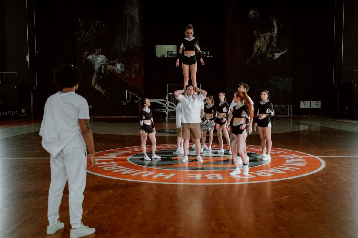Cheer squad holding a shoulder-stand stunt on a gym court
